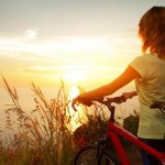 girl with a bicycle looking at the sunset